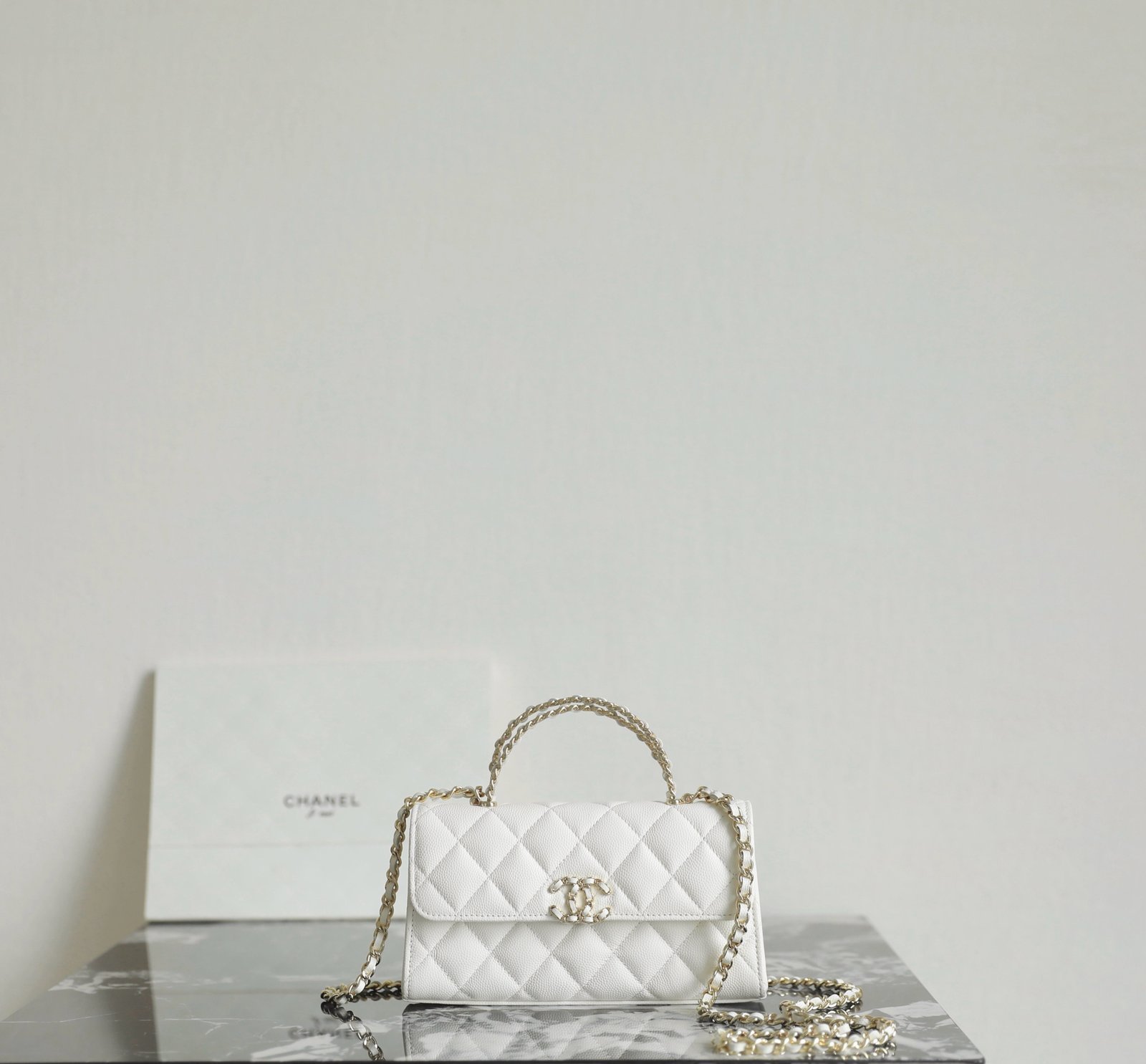 White Chanel bag detail showing crisscross top handle, flap shape, caviar leather grain, and light gold Chanel hardware